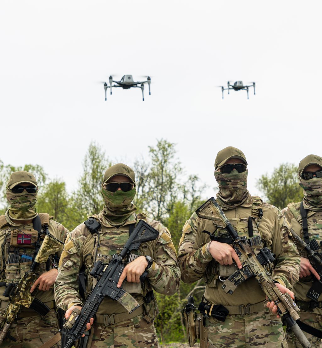 Fire maskerte kystjegere med våpen. I luften over dem svever to droner.