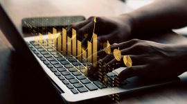 hender som skriver på en laptop mens det dukker opp grafer og økonomiske figurer over tastaturet
