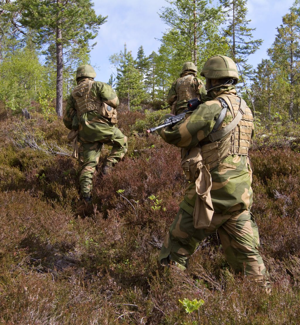 Tre bevæpnede soldater går i lyngen på vei oppover en ås.