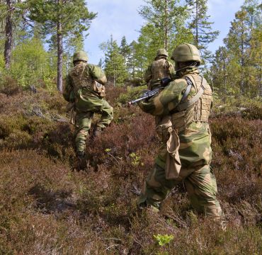 Tre bevæpnede soldater går i lyngen på vei oppover en ås.