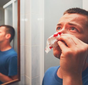 Ung mann på badet. Holder papir med bloflekker foran nesa.