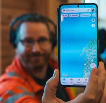 Mann holder opp en mobiltelefon med kart.