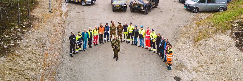 Mange mennesker i ulike uniformer står i en halvsirkel rundt en soldat