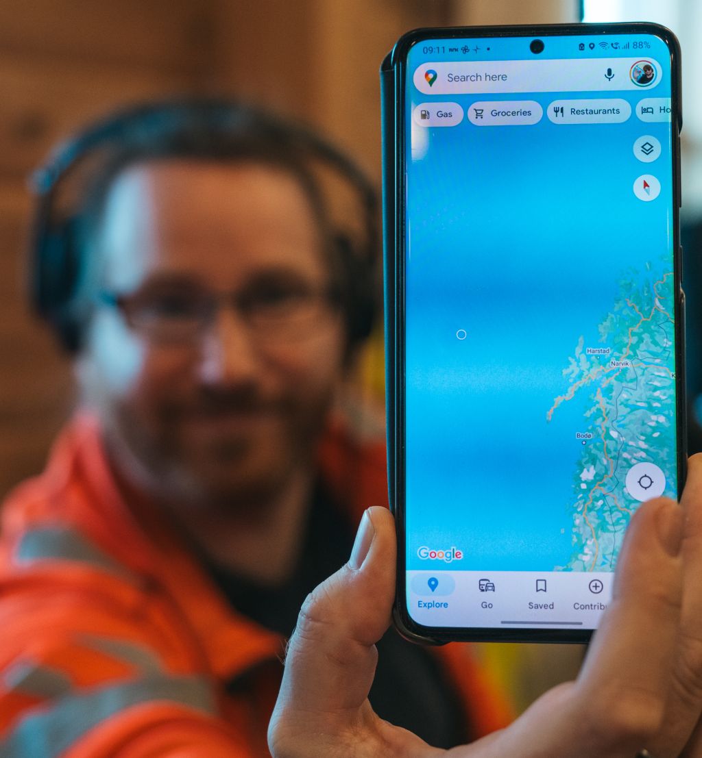 Mann holder opp en mobiltelefon med kart.