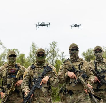 Fire maskerte kystjegere med våpen. I luften over dem svever to droner.