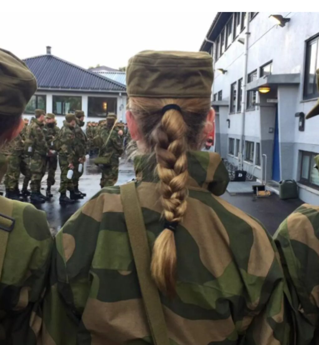 Vi ser ryggene til tre kvinner i hærens militære kamuflasjeuniform. de står skulder til skulder og alle tre har lange fletter som henger ned.