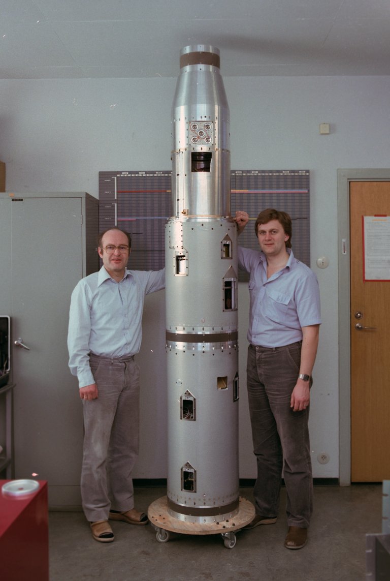 to forskere poserer ved siden av en rakett