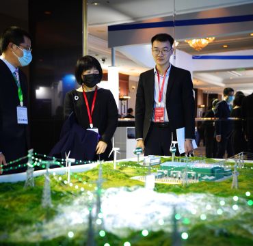 Tre personer ved en installasjon som viser noen strømmaster og det som trolig er en kraftstasjon eller trafo.