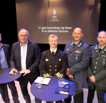 Fem menn står på en scene og ser i kamera