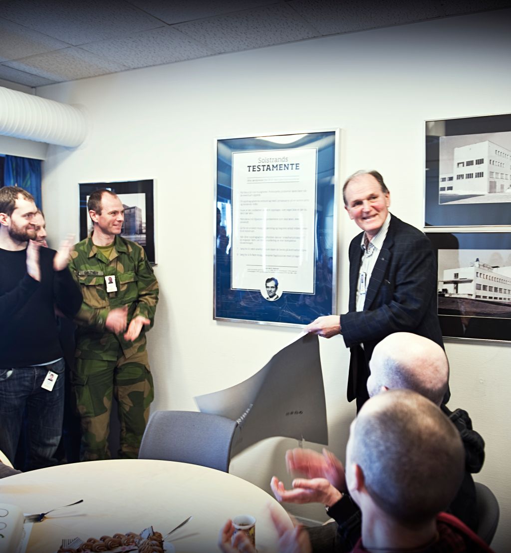 En eldre mann avduker en stor plakat i glass og ramme mens andre står rundt og klapper