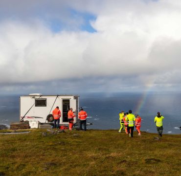 En rekke forskere står ved en skaphenger. De har gule og oransje arbeidsklær på seg.